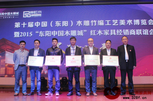 答謝晚宴上，品牌紅木家具經(jīng)銷商聯(lián)盟執(zhí)行主席石立峰（右一）和品牌紅木家具經(jīng)銷商聯(lián)盟發(fā)起人、弘木傳媒CEO林偉華（左一）為新明紅木（圖中）頒發(fā)協(xié)辦單位牌匾