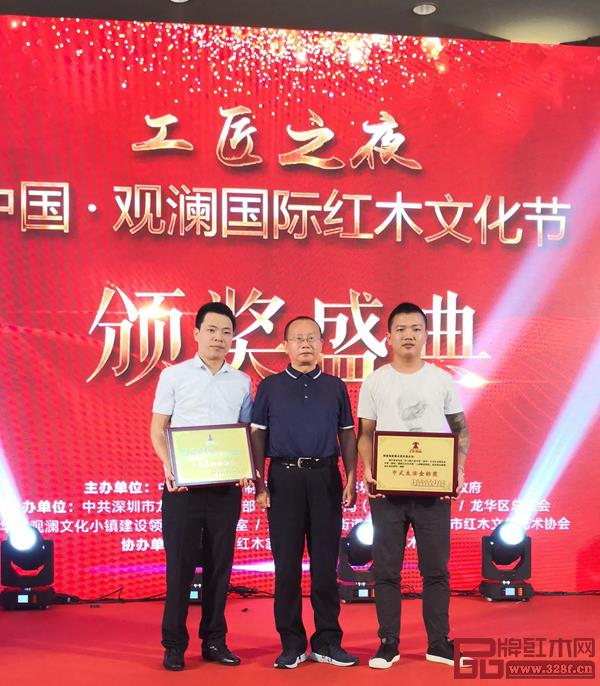 故宮博物院研究員、明清宮廷家具專家周京南（中）為第六屆中國（深圳）國際紅木藝術(shù)展中式生活金標(biāo)獎(jiǎng)?lì)C發(fā)獎(jiǎng)牌，孔連紅木總經(jīng)理李金龍（左）上臺(tái)領(lǐng)獎(jiǎng)