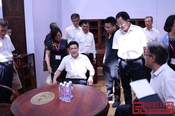 深圳市委常委、龍華區(qū)委書記余新國親身體驗(yàn)孔連紅木展館現(xiàn)場的老撾大紅酸枝茶臺(tái)，并對孔連紅木的珍品給予了高度評價(jià)