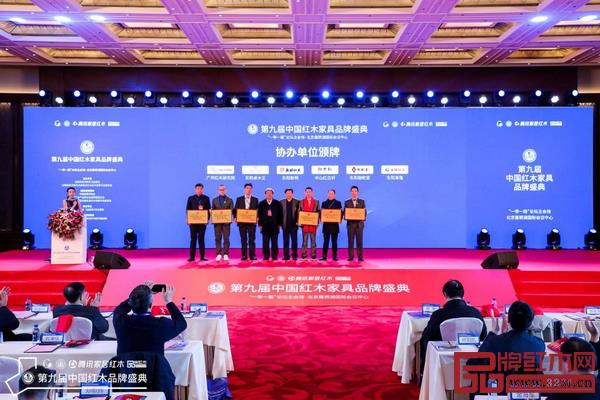 國(guó)家文物局原副局長(zhǎng)張柏（左四）、全國(guó)工商聯(lián)第十一屆執(zhí)委宋建文（右四）為第九屆中國(guó)紅木家具品牌盛典協(xié)辦單位東陽(yáng)新明、中山紅古軒、東陽(yáng)卓木王、東陽(yáng)御乾堂、廣作紅木研究院、東陽(yáng)海強(qiáng)頒牌