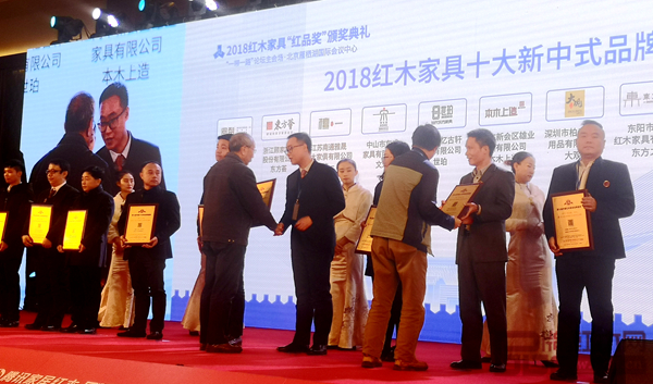 雄業(yè)·本木上造榮獲“2018紅木家具十大新中式品牌”，營銷總監(jiān)符敏捷（右四）上臺接受全聯(lián)藝術(shù)紅木家具專業(yè)委員會專家顧問、中國紅木家具技術(shù)專家曹新民的授牌