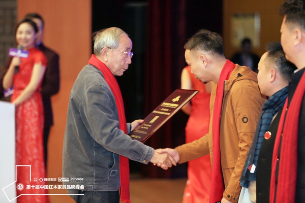 中國紅木家具技術(shù)專家曹新民（左一）為善者文化頒發(fā)“2019特具影響力紅木家具幕后品牌”獎牌，善者文化董事長關(guān)俊銘上臺領(lǐng)獎